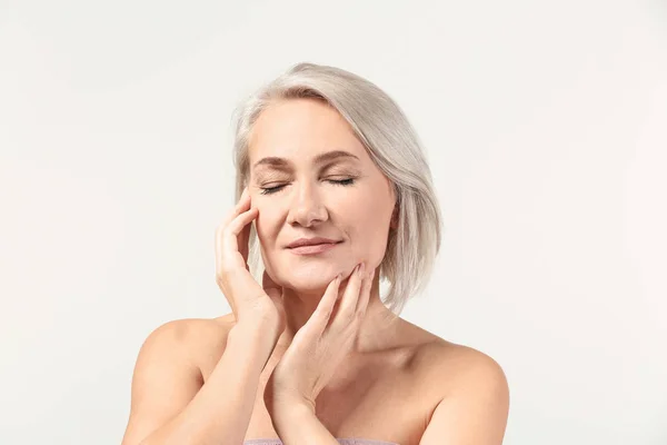 Mujer madura dándose masaje facial sobre fondo claro — Foto de Stock