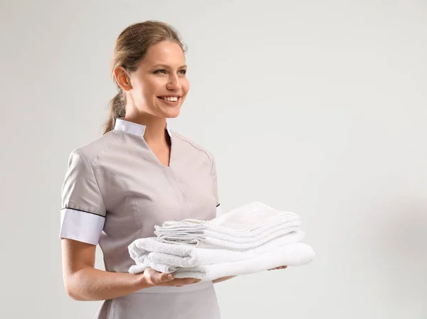 Portrait of beautiful female housekeeper with clean towels on white background — Stock Photo, Image