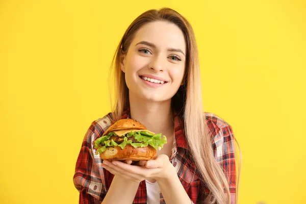 Beautiful young woman with tasty burger on color background — Stock Photo, Image