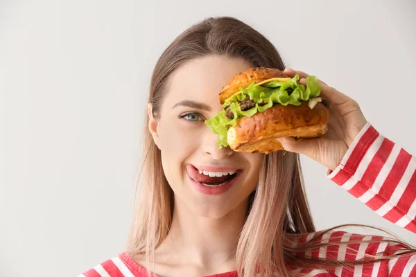 Jovem feliz bonita com hambúrguer saboroso no fundo claro — Fotografia de Stock