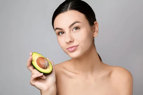 Portrait of beautiful woman with avocado on grey background — Stock Photo, Image