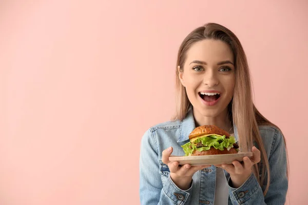 Hermosa joven feliz con sabrosa hamburguesa en el fondo de color — Foto de Stock