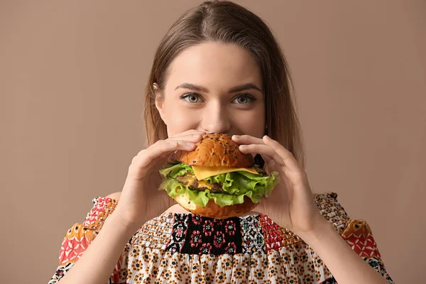 Schöne junge Frau isst leckeren Burger auf farbigem Hintergrund — Stockfoto
