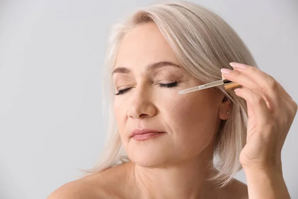 Mujer madura aplicando suero facial sobre fondo claro — Foto de Stock