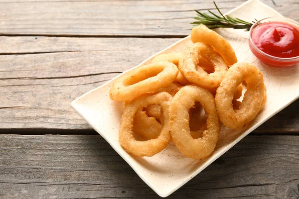 Plate with tasty onion rings and sauce on wooden table — Stock Photo, Image