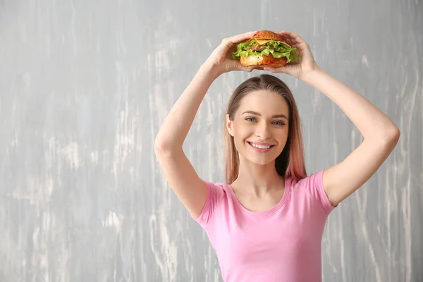 Beautiful young woman with tasty burger on grey background — Stock Photo, Image