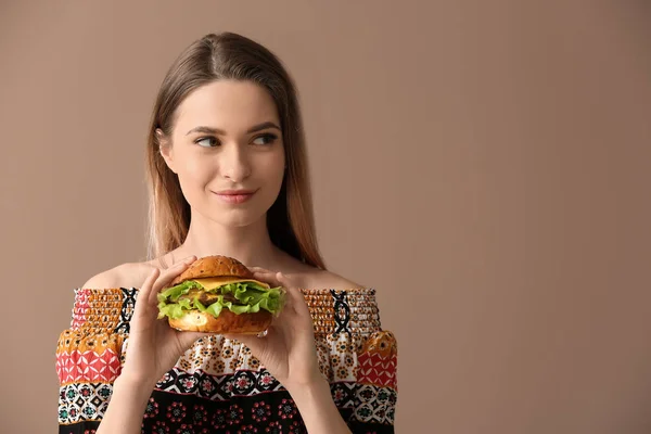 Beautiful young woman with tasty burger on color background — Stock Photo, Image