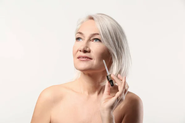 Mature woman applying face serum on light background — Stock Photo, Image