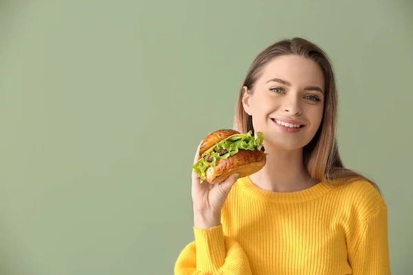 色の背景上のおいしいハンバーガーと美しい若い女性 — ストック写真
