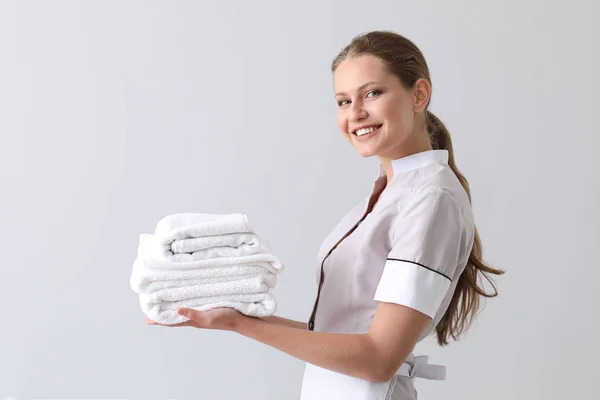 Schöne Haushälterin mit sauberen Handtüchern auf hellem Hintergrund — Stockfoto