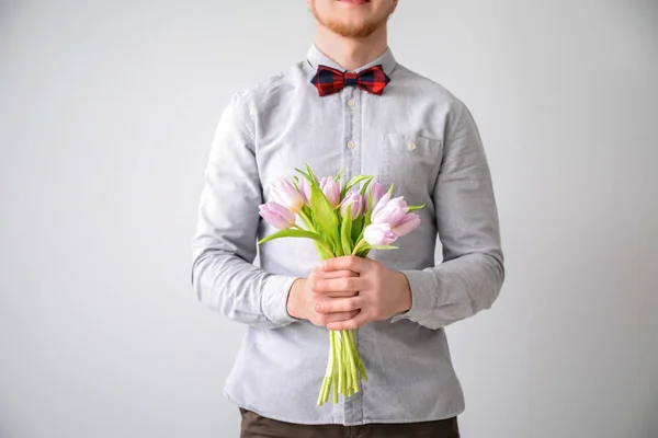 Young man with bouquet of flowers on light background. 8 March celebration