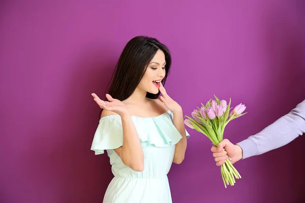 Mujer recibiendo flores para 8 Marzo de hombre joven sobre fondo de color — Foto de Stock