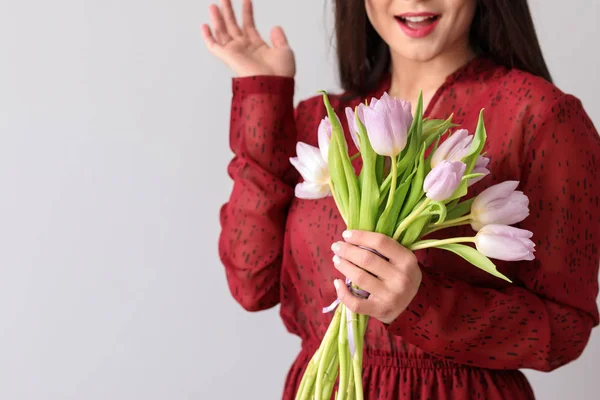 Young woman with bouquet of flowers on light background. 8 March celebration — Stock Photo, Image