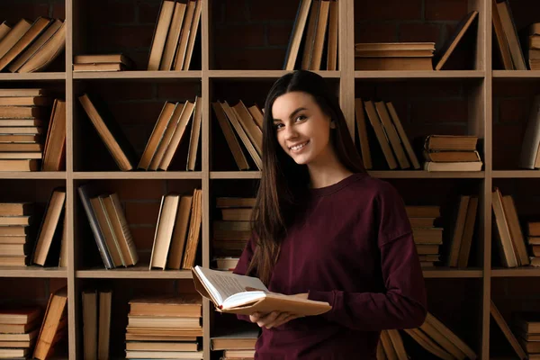 Πορτρέτο του όμορφη νεαρή γυναίκα με το βιβλίο στη βιβλιοθήκη — Φωτογραφία Αρχείου
