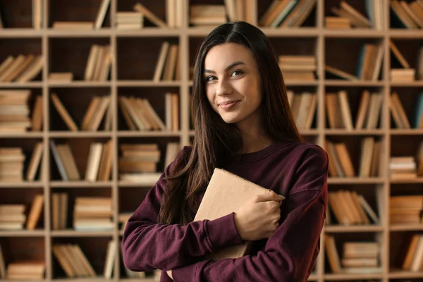 Πορτρέτο του όμορφη νεαρή γυναίκα με το βιβλίο στη βιβλιοθήκη — Φωτογραφία Αρχείου