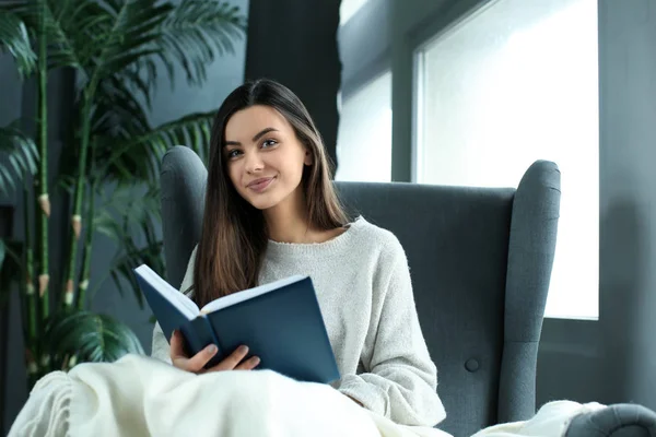 Beautiful young woman reading book at home — Stock Photo, Image