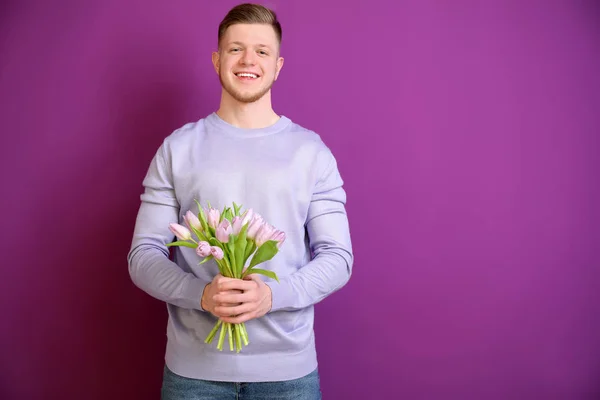 Young man with bouquet of flowers on color background. 8 March celebration