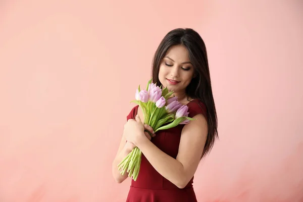 Young woman with bouquet of flowers on color background. 8 March celebration — Stock Photo, Image