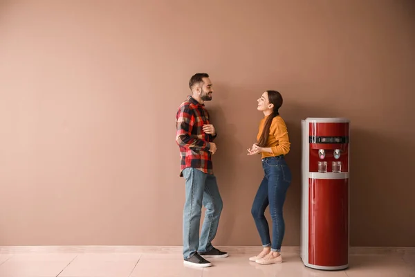 Hombre y mujer cerca del enfriador de agua contra la pared de color — Foto de Stock