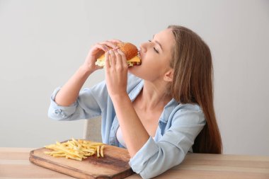 Genç kadın lezzetli burger patates kızartması ile masada yemek