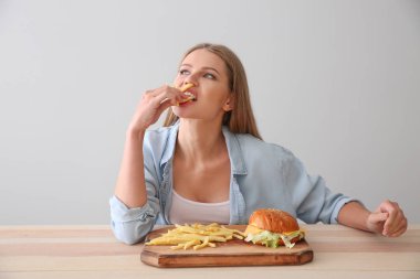 Genç kadın lezzetli burger patates kızartması ile masada yemek