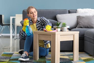 Güzel bir kadın evdeki masayı temizliyor.