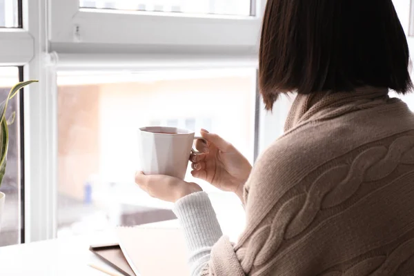 Young woman with cup of hot tea near window at home — Stock Photo, Image