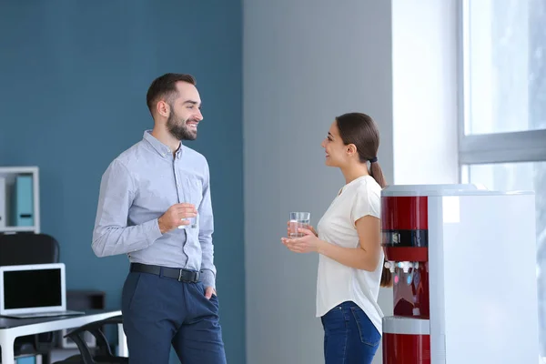 Colleagues drinking water from cooler in office