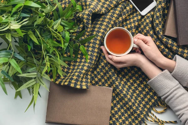 Vrouwelijke handen met kop hete thee en boek op Plaid — Stockfoto