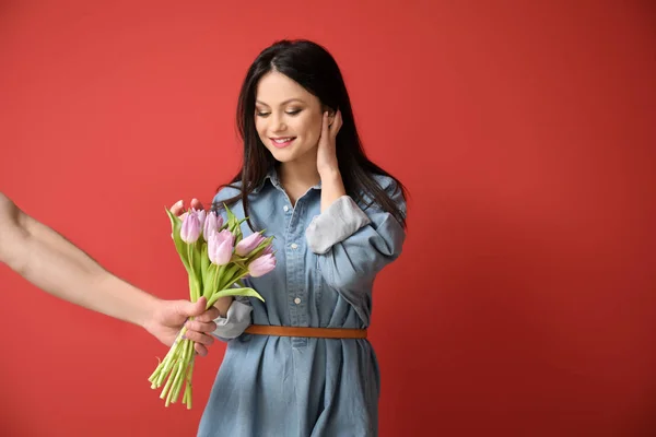 Woman receiving flowers for 8 March from young man on color background — Stock Photo, Image