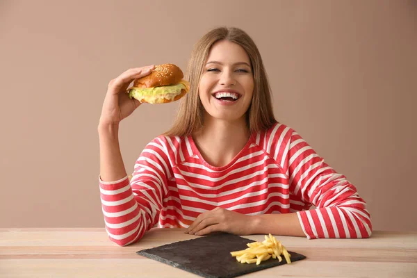 Junge Frau isst leckeren Burger am Tisch — Stockfoto