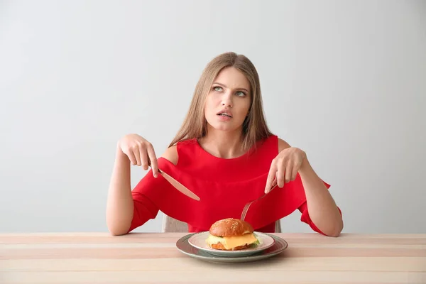 Thoughtful woman with tasty burger at table — Stock Photo, Image