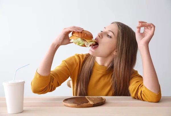 Mladá žena jíst chutné burger u stolu — Stock fotografie