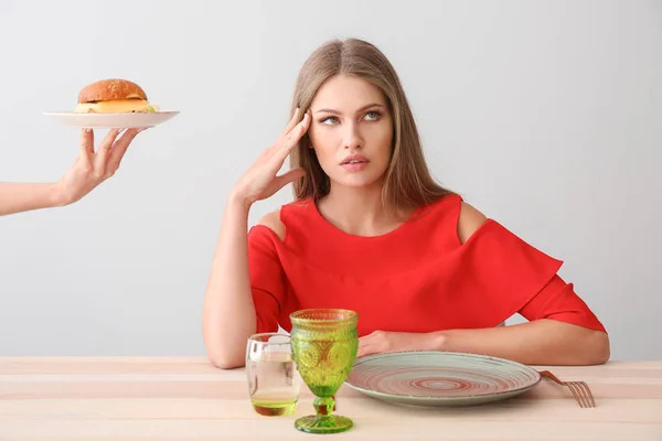 Χέρι που υποδηλώνει νόστιμο burger στη γυναίκα που κάθεται στο τραπέζι — Φωτογραφία Αρχείου