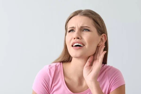 Young woman with hearing problem on light background — Stock Photo, Image