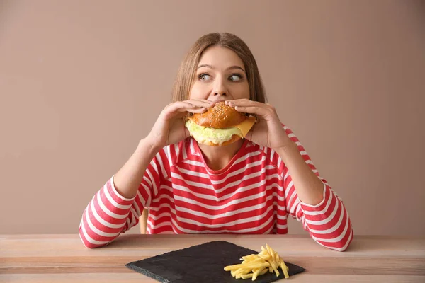Jovem mulher comendo hambúrguer saboroso à mesa — Fotografia de Stock