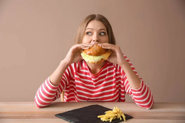 Jonge vrouw smakelijke hamburger eten aan tafel — Stockfoto