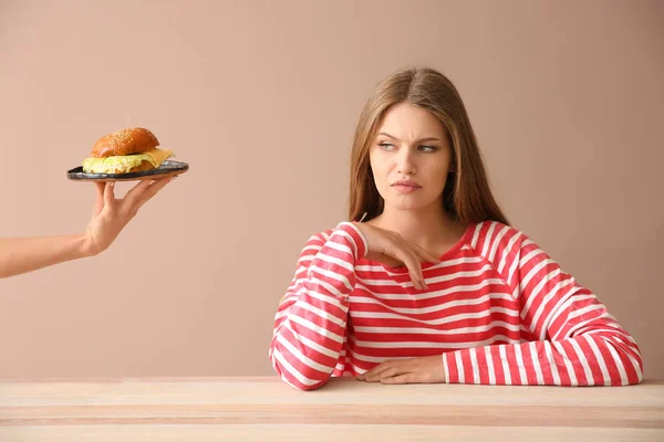 테이블에서 불쾌 하 게 젊은 여자에 게 햄버거를 제안 하는 손 — 스톡 사진