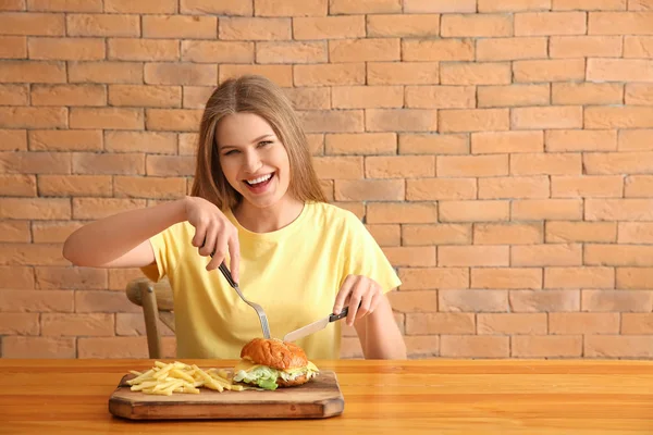 테이블에서 맛 있는 햄버거와 감자 튀김을 먹는 젊은 여자 — 스톡 사진