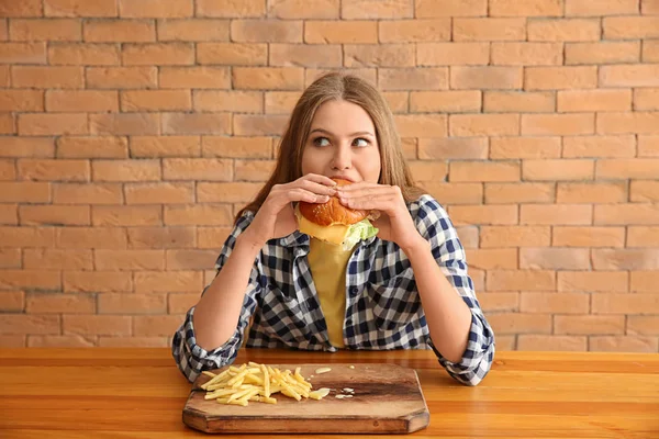 Jonge vrouw smakelijke hamburger met frietjes eten aan tafel — Stockfoto
