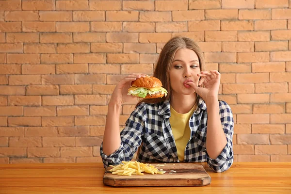 Jonge vrouw smakelijke hamburger met frietjes eten aan tafel — Stockfoto