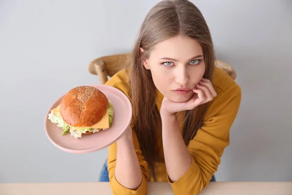 Giovane donna con gustoso hamburger a tavola — Foto Stock