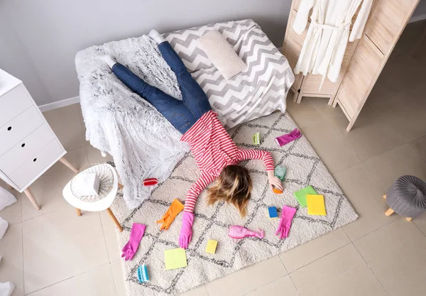 Tired housewife with cleaning supplies lying at home — Stock Photo, Image