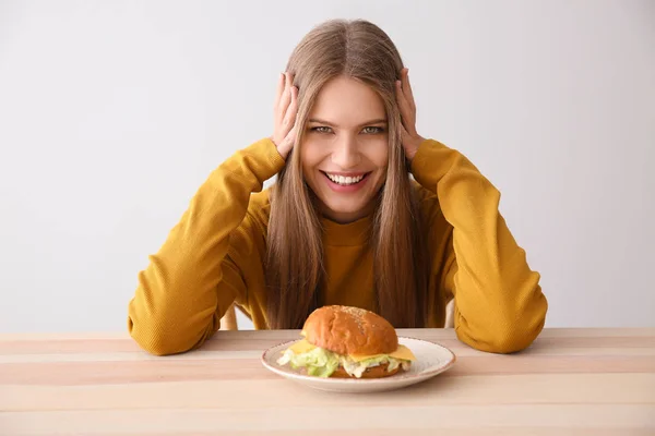 Young woman with tasty burger at table — Stock Photo, Image