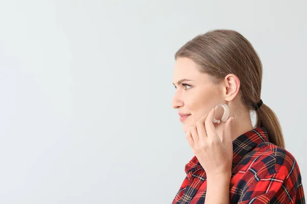 Young woman with hearing aid on light background — Stock Photo, Image