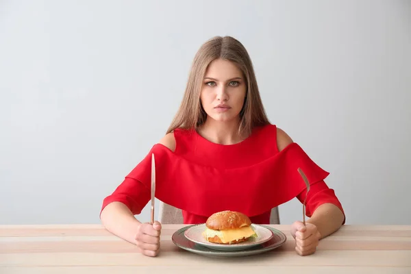 Junge Frau mit leckerem Burger am Tisch — Stockfoto