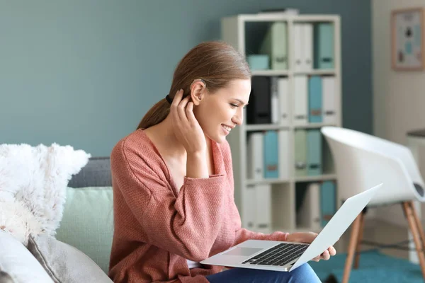 Mujer joven con audífono usando computadora portátil en casa —  Fotos de Stock