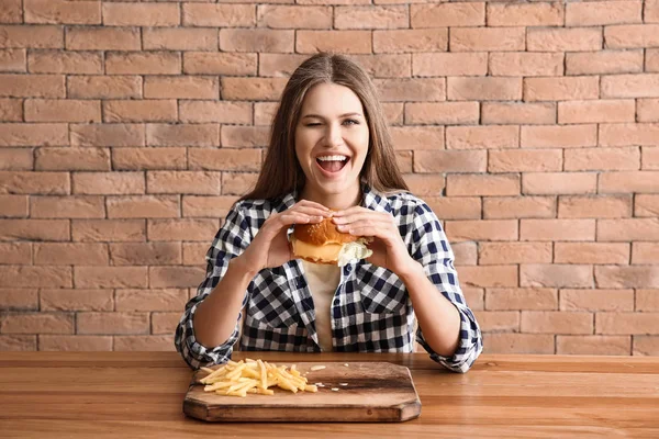 테이블에서 맛 있는 햄버거와 감자 튀김을 먹는 젊은 여자 — 스톡 사진