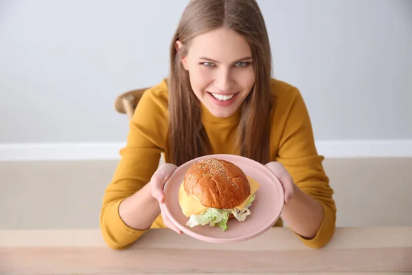 Junge Frau mit leckerem Burger am Tisch — Stockfoto