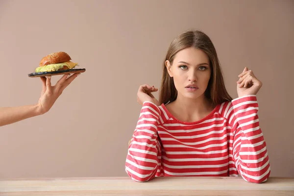 Hand suggesting burger to young woman sitting at table — Stock Photo, Image